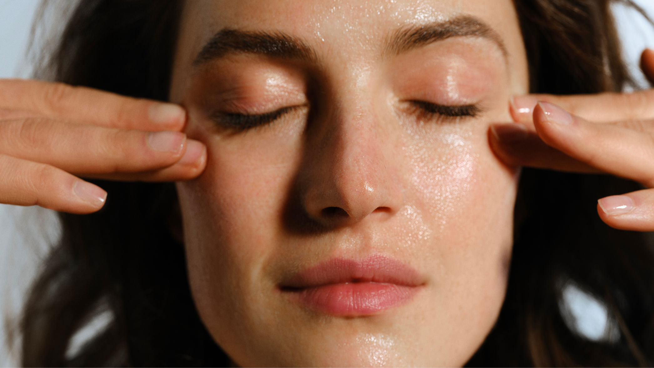 Woman with her eyes closed, application of lotion to cheekbones 